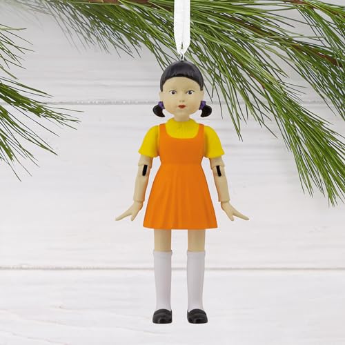 Squid Game Young-hee Doll holiday ornament hanging on a Christmas tree with festive lights.